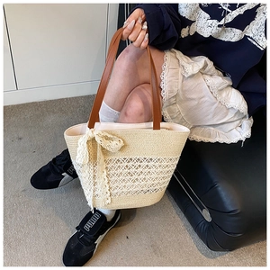 Detail of straw woven tote bag featuring white lace bow and brown leather handle strap