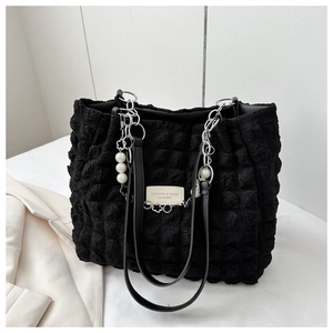 Detail of black pleated tote bag featuring pearl chain strap and leather logo tag