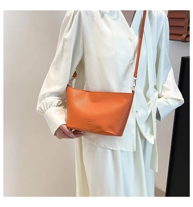 Détail du sac seau orange à texture litchi avec boucle dorée et bandoulière en cuir