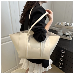 Detail view of large cream tote bag with FASHION text carried by model in indoor setting