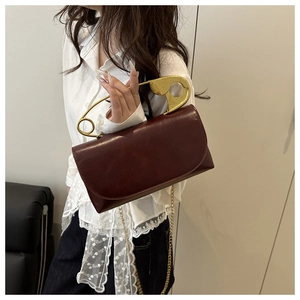 Dettaglio borsa in pelle bordeaux con grande manico a spilla da balia dorata e catena