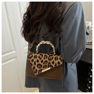 Detail of leopard print crossbody bag with golden metal handle worn over a grey blazer