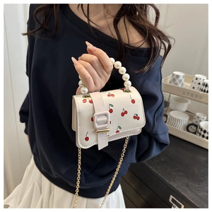 Detail of white mini bag featuring cherry print, large pearl handle and gold chain strap