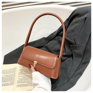 Detail of a brown glossy leather shoulder bag featuring a gold clasp and a structured handle