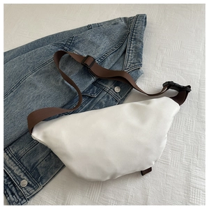 Detail of white crescent waist bag with adjustable brown strap on denim jacket