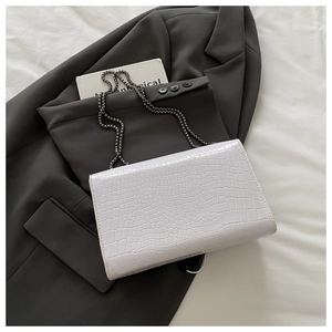 Detailed view of white crocodile pattern flap bag with a metallic chain on a grey blazer