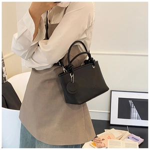 Detail of black lychee texture leather bucket bag with knotted handle and smile pendant