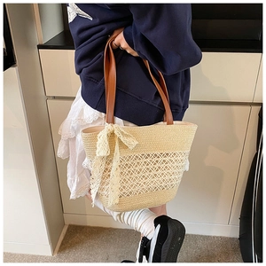 Detail of hollow geometric mesh weaving and brown leather handle on a straw tote bag