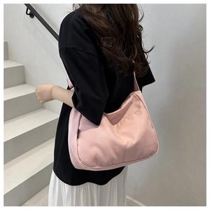Close-up of a pink canvas bucket bag with a wide shoulder strap worn by a model