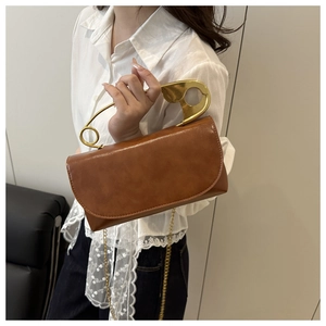 Dettaglio del manico creativo a spilla dorata su borsa a tracolla in pelle marrone
