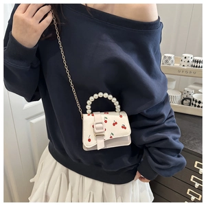 Detail of white mini bag with cherry print, pearl handle and gold chain strap