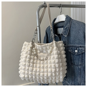 Detail of white bubble textured tote bag with decorative pearl chain and leather label