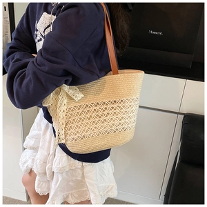 Close-up of woven straw tote bag with white lace bow detail and brown leather straps