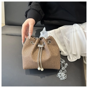 Détail du sac seau tressé marron avec chaîne argentée et pendentif en perle