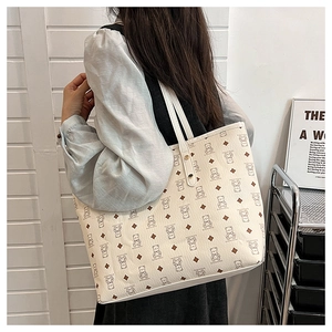 Close-up of beige tote bag with bear patterns and side metal rivets on a shoulder strap