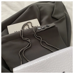 Close-up of white crocodile embossed flap bag with silver chain on grey blazer