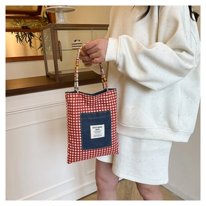 Détail d'un sac cabas à carreaux rouges avec poche en denim et anses tissées colorées