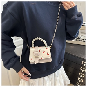 Detail of a mini cherry print crossbody bag with large pearl handle and gold chain