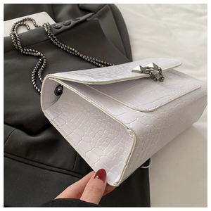 Detail of white crocodile pattern square bag with silver rivets and metal chain strap