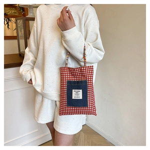 Détail du sac cabas en toile à carreaux rouges avec poche en denim et anse tressée