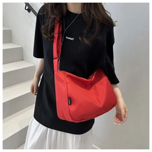 Detail of red crescent nylon crossbody bag with black brand tag on casual casual outfit