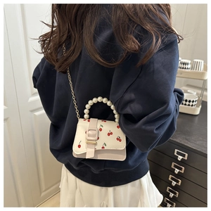 Close-up of a mini cream handbag featuring cherry print and a pearl handle worn by a model
