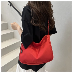 Close-up of bright red large canvas crossbody bag shown on a model against white wall