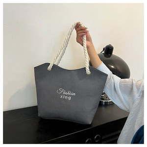 Close-up of gray canvas tote bag featuring white rope handles and Fashion xing embroidery