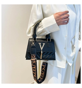 Detailed view of black quilted crossbody bag with gold V logo and metal tassel accent