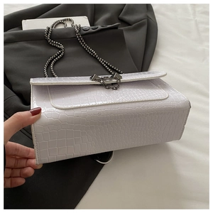Detail of white crocodile embossed leather bag with dark grey metal chain and buckle