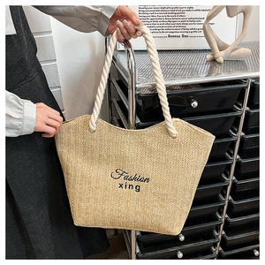 Close-up of beige woven straw tote bag with white rope handles and black fashion embroidery