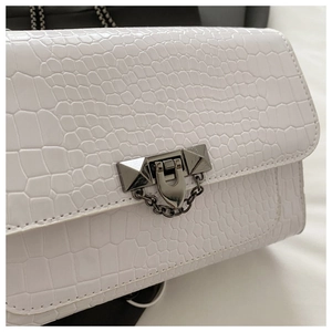 Detail of white crocodile texture leather handbag with silver metallic turn-lock and rivets