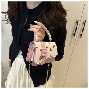 Close-up of pink and cream crossbody bag with pearl handle and cherry print details