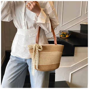 Close-up of woven straw tote bag featuring white lace bow and brown leather shoulder strap