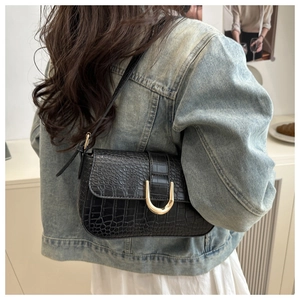 Close-up of black crocodile-embossed shoulder bag with a gold U-shaped metal buckle