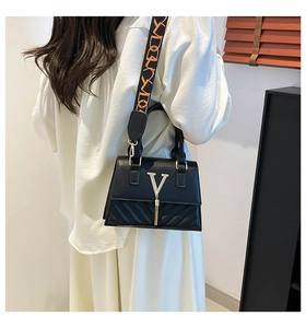 Detail of black leather handbag featuring golden V logo, tassel, and textured stitching