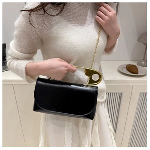 Dettaglio borsa in pelle nera con un grande manico a forma di spilla da balia dorata