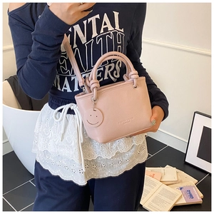 Pink lychee grain bucket bag featuring a smile charm and adjustable strap shown on model