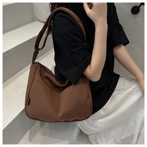 Detail of a brown canvas crossbody bag with wide shoulder strap and brand label