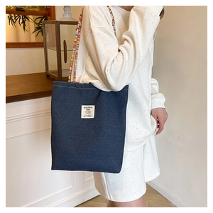 Détail du sac cabas en jean bleu avec poignée tissée colorée et étiquette à l'épaule