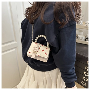 Detail of white handbag with cherry print, pearl bead handle, and gold chain strap