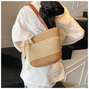 Detail of striped straw tote bag featuring a delicate cream lace bow and leather strap