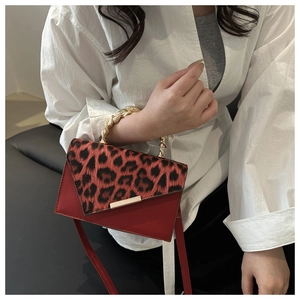Detail of red crossbody bag with leopard print flap and gold chain strap on white shirt
