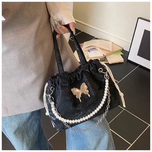 Detail of black pleated handbag with gold butterfly accent and elegant pearl strap