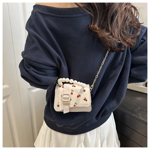 Detail of white mini crossbody bag with red cherry print and faux pearl top handle strap