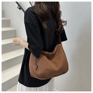 Rear view of a large brown canvas crossbody bag worn by a model in a modern urban setting