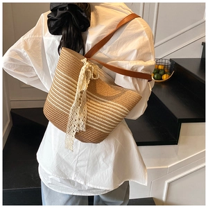 Detail of striped straw bag featuring elegant white lace bow and brown leather shoulder strap