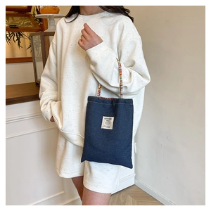Détail du sac cabas en denim avec des poignées tressées colorées et une étiquette tissée