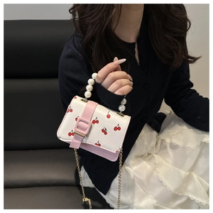 Detailed view of cherry print small square bag with pearl handle and metal chain strap
