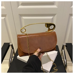 Dettaglio di una borsa in pelle marrone con manico dorato a forma di spilla da balia